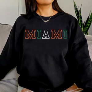 May include: Black sweatshirt with the word "MIAMI" in orange, green, and white outlined letters.