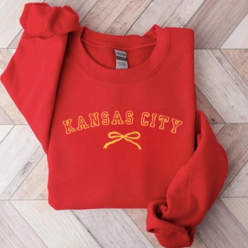 May include: Red sweatshirt with a yellow embroidered design that says "KANSAS CITY" with a yellow bow underneath.