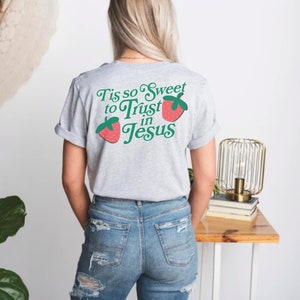 May include: Gray t-shirt with the text "Tis so Sweet to Trust in Jesus" in green and red lettering with two red strawberries with green leaves on either side of the text.