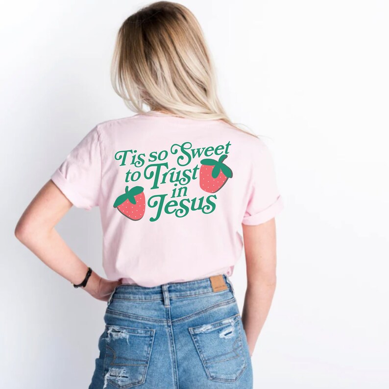 May include: Pink t-shirt with a green and red strawberry graphic and the text "Tis so Sweet to Trust in Jesus".