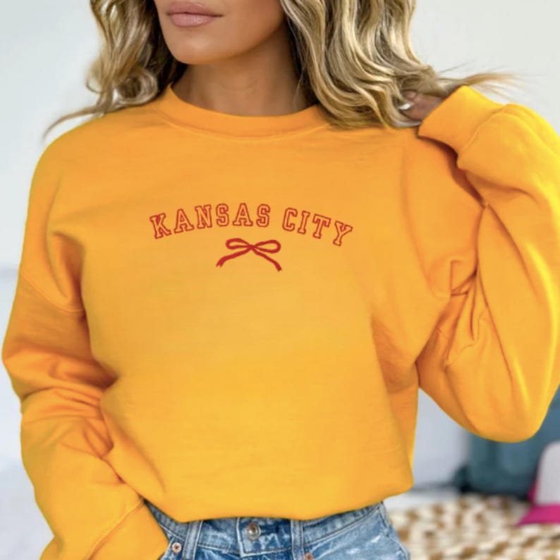 May include: A yellow sweatshirt with the text "KANSAS CITY" in red with a red bow underneath.