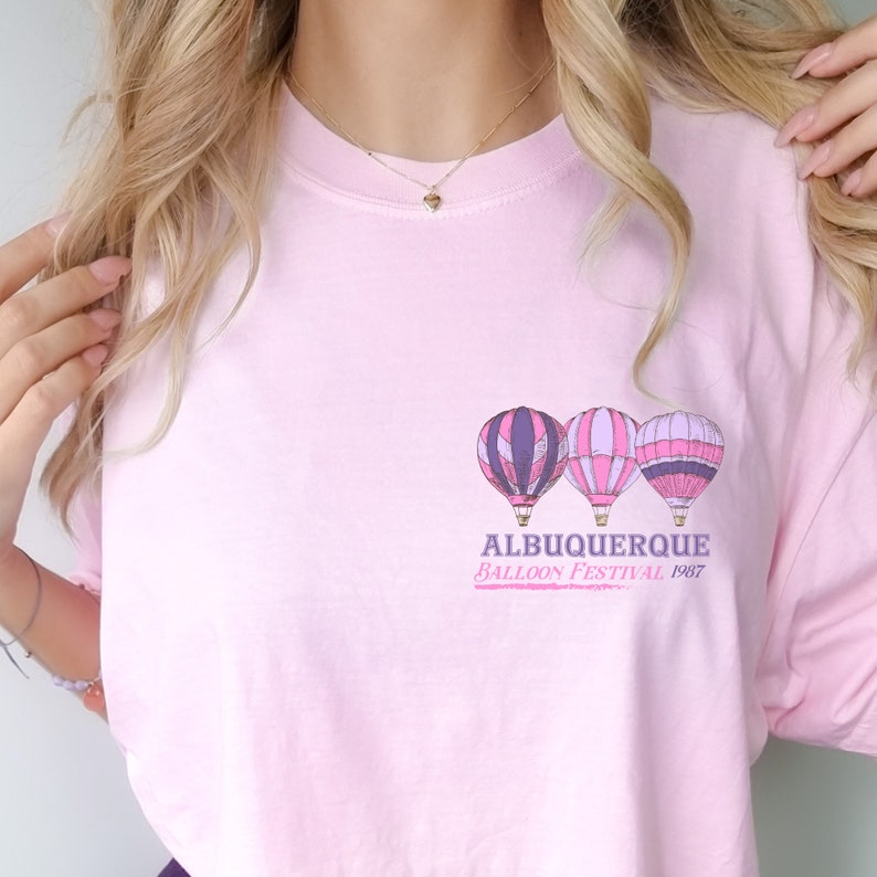 Op de afbeelding: Roze T-shirt met een afbeelding van drie luchtballonnen en de tekst "Albuquerque Balloon Festival 1987".