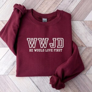 May include: Burgundy sweatshirt with white text that reads "WWJD He Would Love First".