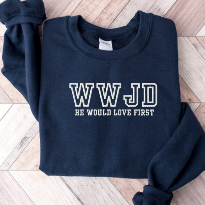 May include: Navy blue sweatshirt with white text that reads "WWJD HE WOULD LOVE FIRST".