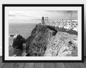 May include: A black and white photograph of a lighthouse on a cliff overlooking the ocean. A wooden bridge connects the lighthouse to the mainland. The bridge is supported by cables.