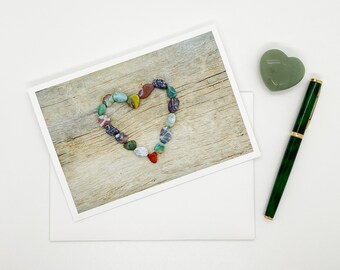 May include: A heart shape made of colorful stones on a wooden surface. The stones are various shades of green, red, brown, and white.