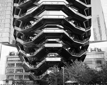 May include: A black and white photo of a modern, multi-level structure with a honeycomb design. People are sitting on chairs in front of the structure.