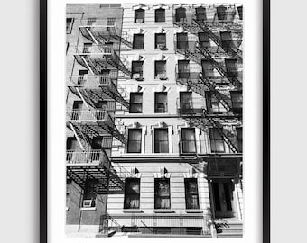 May include: Black and white photograph of a brick building with fire escapes. The building has many windows and is in a city setting.