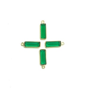 May include: Four emerald green glass rectangle charms with gold-toned metal loops. The charms are arranged in a cross shape.