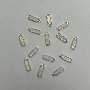 May include: A collection of 12 silver and opal rectangular pendant charms. The charms are all the same size and shape, and they have a silver loop at the top for attaching to a necklace or bracelet.