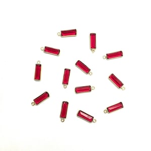 May include: A scattering of red glass rectangle charms with gold jump rings. The charms are scattered on a white background.