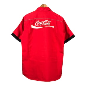 May include: Red short-sleeved shirt with black trim on the sleeves and a white Coca-Cola logo on the back.