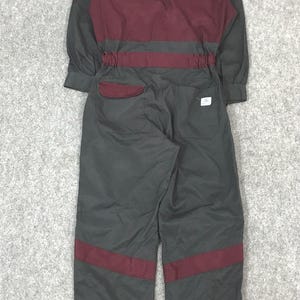 May include: A gray and maroon work jumpsuit with long sleeves. The back of the jumpsuit features the word "FUSO" and a logo. Maroon accents are on the shoulders, waist, and legs.