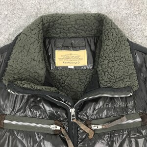 Może przedstawiać: Czarna pikowana kurtka z kołnierzem z ciemnozielonego sztucznego futra. Kurtka posiada zapięcie na zamek błyskawiczny i etykietę z napisem "EQUIPMENT-TYPE-AVIREX FLIGHT GARMENT SPECIFICATION HIGH SPEED LOW LEVEL FLIGHT AVIREX LTD".