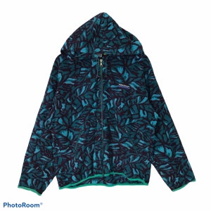 Puede incluir: Una sudadera con capucha de cremallera de color azul verdoso con ribete verde y un patrón abstracto negro y azul verdoso. La sudadera tiene una capucha con cordón y cierre de cremallera. El nombre de la marca "Helly Hansen" está impreso en la parte delantera de la sudadera.