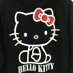 May include: Black hoodie with a white outline of Hello Kitty wearing a red bow. The text "HELLO KITTY" is printed in white below the image.