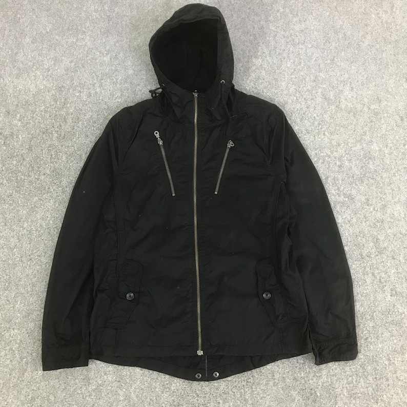May include: A black hooded jacket featuring a full-length front zipper, two diagonal zippered chest pockets, and two lower pockets with buttoned flaps. The jacket includes a drawstring hood and long sleeves with cuffs, providing a functional design.