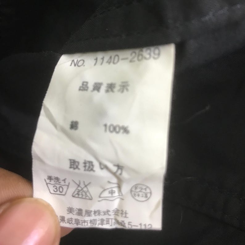 May include: A white rectangular garment care label attached to a black fabric surface. The label features the text NO. 1140-2639, the Japanese characters for quality representation, 100% cotton, and care instructions including symbols for hand washing.