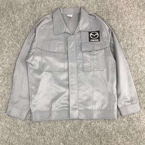 May include: A grey work jacket with a zip fastening and two large pockets on the front. The jacket has a Mazda logo patch on the right chest.