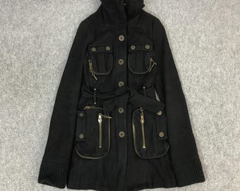 May include: Black jacket with multiple pockets, zippers, and a belt. The jacket has a high collar, button closures, and ribbed cuffs. The pockets have zipper closures and decorative buttons. The jacket is made of a dark fabric.