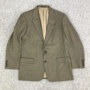 May include: A brown and black checked blazer with a two-button fastening and two front pockets. The blazer features a tan lining and button details on the sleeves. The fabric has a subtle pattern.