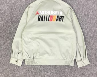 May include: A light green jacket with the "MITSUBISHI RALLI ART" logo on the back. The logo features red, orange, and yellow stripes. The jacket has a button closure and elastic cuffs.