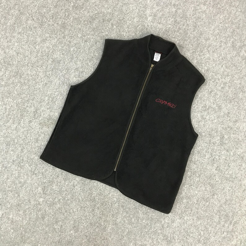 以下が含まれることがあります： 黒色のフリースベスト。フルレングスのジッパーと小さな赤い刺繍ロゴが付いています。 ベストはスタンドカラーとノースリーブのデザインです。 Gramicciのロゴが右胸に表示されています。