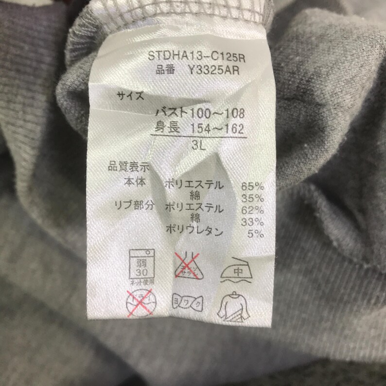 May include: Close-up of a clothing tag with Japanese text and washing symbols. The tag includes the product code STDHA13-C125R and size 3L. Fabric composition is listed as 65% polyester, 35% cotton, 62% polyester, 33% cotton, and 5% polyurethane.