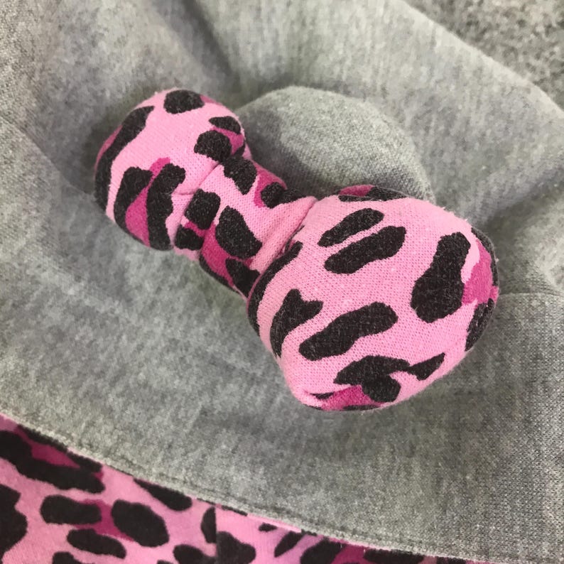 May include: A pink and black patterned dog toy shaped like a dumbbell. The toy is made of soft fabric and rests on a gray surface. The pattern is a leopard print.