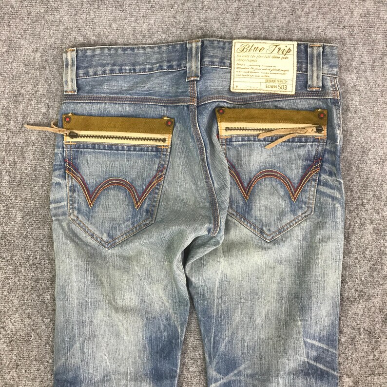 K&ouml;nnte beinhalten: Hellblaue Jeans mit einzigartigen Taschen-Details. Die Jeans hat braune Wildleder-&auml;hnliche Akzente an den Ges&auml;&szlig;taschen mit Rei&szlig;verschl&uuml;ssen und Leder-Z&uuml;gen. Die Ges&auml;&szlig;taschen haben ein markantes wellenf&ouml;rmiges Nahtdesign. Mit einem "Blue Trip" Label.