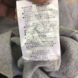 May include: Close-up of a white tag with Japanese text and the text "FOR SALE IN JAPAN ONLY". The tag is attached to a gray fabric. The tag also includes the text "&copy;1976, 2013 SANRIO CO. LTD".