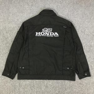 May include: Black jacket with the Honda Grand-Prix Racing Team logo in white on the back. The jacket has a collared neckline, two front pockets, and button closures. The jacket is made of a textured fabric.