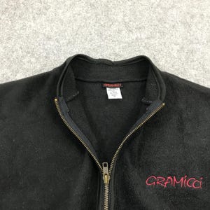 以下が含まれることがあります： フルジップと前面に赤い「Gramicci」ロゴが刺繍された黒いフリースジャケット。 ジャケットはハイカラーで、「Gramicci」ロゴのタグが付いています。 ジッパーは金色です。