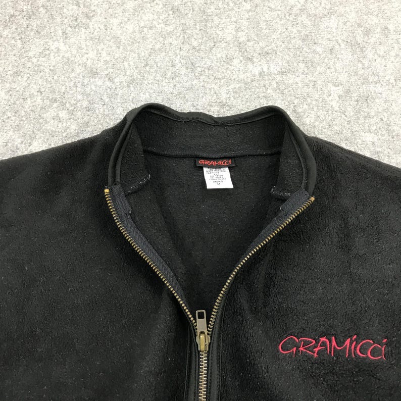 以下が含まれることがあります： フルジップと前面に赤い「Gramicci」ロゴが刺繍された黒いフリースジャケット。 ジャケットはハイカラーで、「Gramicci」ロゴのタグが付いています。 ジッパーは金色です。