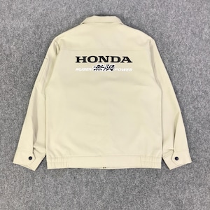 Puede incluir: Chaqueta beige con el logo de Honda y "Mugen 無限 power" impreso en negro en la espalda. La chaqueta tiene una parte delantera abotonada, dos bolsillos delanteros y puños abotonados. La chaqueta está hecha de un material duradero.