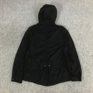 May include: A solid black hooded jacket featuring long sleeves with buttoned cuffs, a full-length front zipper, and a small horizontal tab detail with two buttons positioned at the lower center back of the garment, providing a structured appearance.