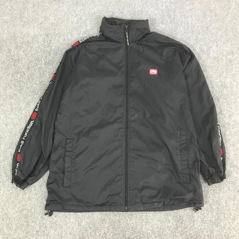 May include: A black zip-up jacket featuring a high collar and long sleeves with red and white Ecko Function branding along the arms. The jacket includes a small red Ecko logo on the left chest, a full-length front zipper, and adjustable drawstrings.