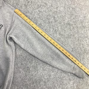 Może przedstawiać: Szary rękaw bluzy z drewnianą linijką o długości 61 cm. Rękaw wykonany jest z miękkiej, szarej tkaniny. Linijka jest ż&oacute;łta z czarnymi oznaczeniami.