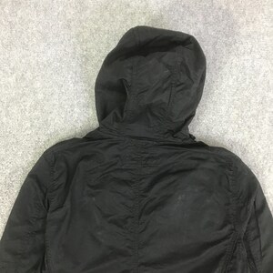 May include: A solid black hooded jacket featuring a structured hood with visible seam detailing, long sleeves, and a lightweight fabric construction. The garment displays a plain, matte black finish throughout the back and hood area.