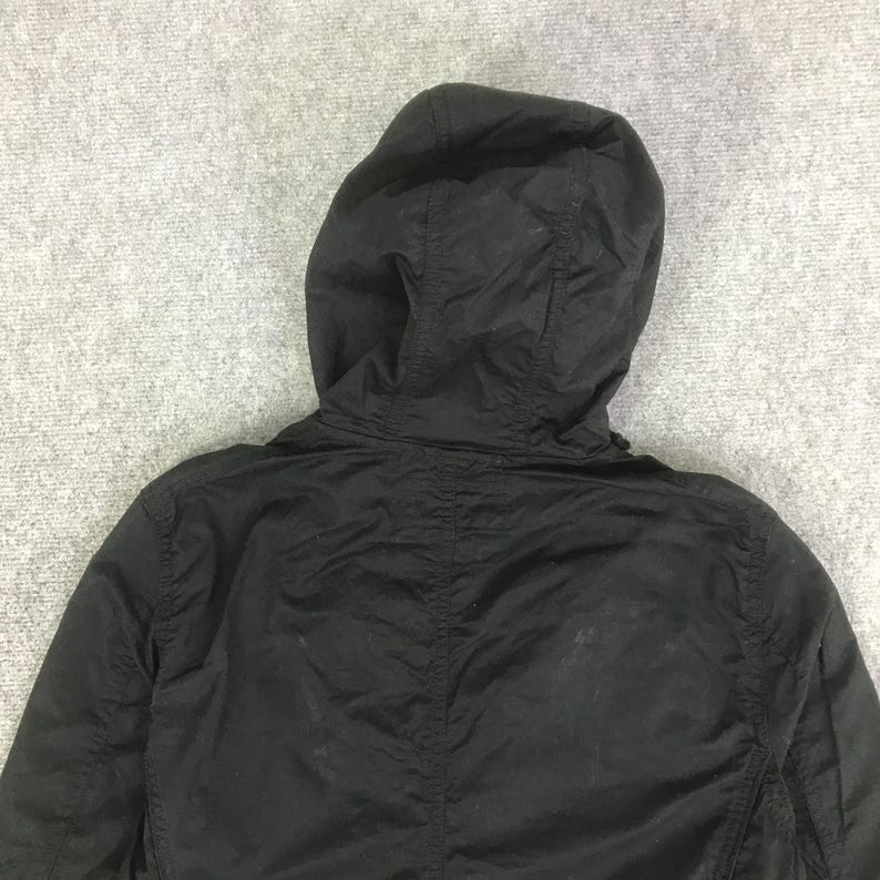 May include: A solid black hooded jacket featuring a structured hood with visible seam detailing, long sleeves, and a lightweight fabric construction. The garment displays a plain, matte black finish throughout the back and hood area.