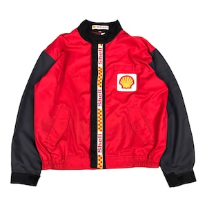 May include: A red and black jacket with a zipper closure and a Shell logo on the front. The jacket has a black stripe down the front with the word "Shell" repeated in white.