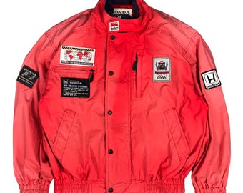 May include: A red Honda racing jacket with multiple patches, including a world map patch, a Honda F1 team patch, and a Honda logo patch. The jacket has a zipper closure and a button-up front.