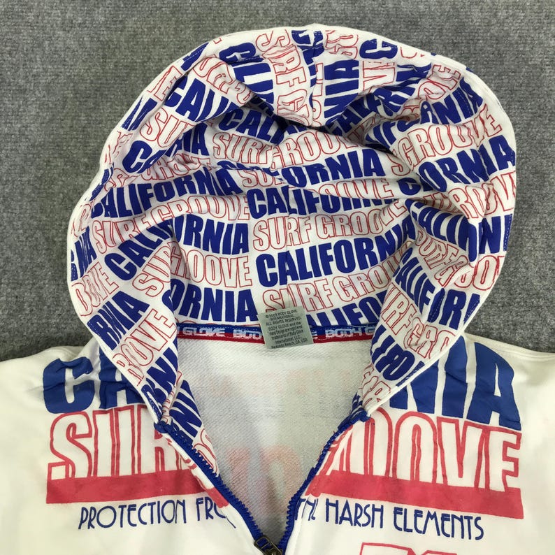 以下が含まれることがあります： フードと胸に青と赤の「カリフォルニアサーフグルーヴ」のデザインが施された、白いジップアップパーカー。 パーカーはフルジッパーで、「Protection From The Harsh Elements」の文字が特徴です。