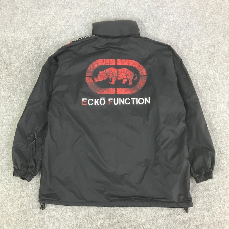 May include: A black jacket featuring a high collar and long sleeves with elastic cuffs. The back displays a large red distressed graphic of a rhinoceros inside an oval frame, with the white text ECKO FUNCTION printed directly below the logo.