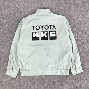 Könnte beinhalten: Hellgrüne Jacke mit dem Text "TOYOTA HKS" in Schwarz auf dem Rücken. Die Jacke hat einen Knopfverschluss, lange Ärmel und einen gerippten Saum. Die Jacke ist aus leichtem Material gefertigt.