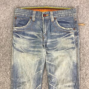 K&ouml;nnte beinhalten: Verblasste blaue Jeans aus Denim mit einem Used-Look. Die Jeans haben ein klassisches F&uuml;nf-Taschen-Design, einen Knopf- und Rei&szlig;verschluss und orangefarbene Nahtdetails. Der Bund hat ein gelb-oranges Innenfutter.
