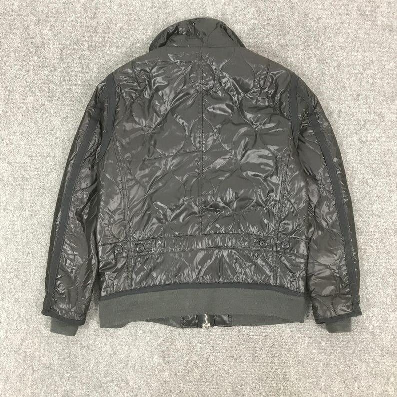 Może przedstawiać: Czarna pikowana kurtka ze st&oacute;jką i prążkowanym dołem. Kurtka posiada wz&oacute;r w romby i zapięcie na zamek błyskawiczny. Rękawy mają czarne paski po bokach. Kurtka wykonana jest z błyszczącego materiału.