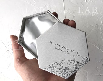 May include: White hexagonal box with a white satin lining. The box has a black floral design and the text "Flowers from Home by Nat & Dea" printed on the lid.