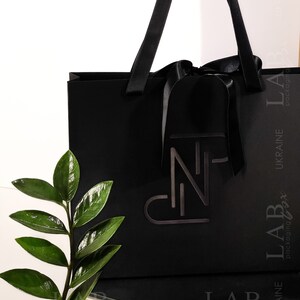 Puede incluir: Una bolsa de compras negra con un lazo negro y asas. La bolsa tiene un logotipo blanco que dice "LAB packaging box" y "UKRAINE" impreso en el lateral.
