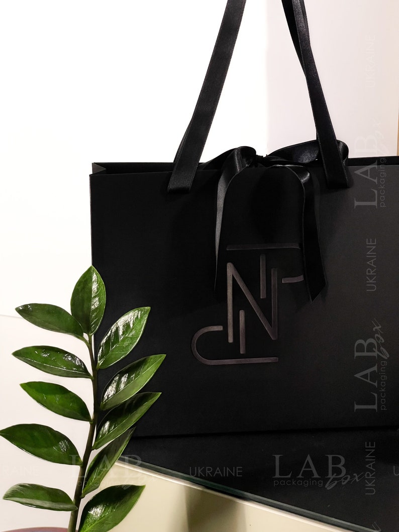 Puede incluir: Una bolsa de compras negra con un lazo negro y asas. La bolsa tiene un logotipo blanco que dice "LAB packaging box" y "UKRAINE" impreso en el lateral.